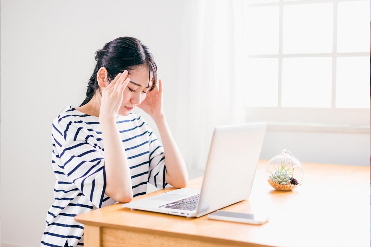 ノートパソコンを前に頭を抱える女性。履歴書作成で悩み、ミスや失敗に不安を感じている様子を表現