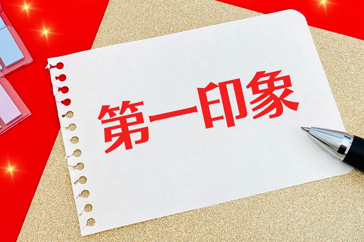 赤い背景に『第一印象』と書かれた紙とペン。履歴書は面接官に与える第一印象を左右する重要な武器であることを象徴するイメージ。